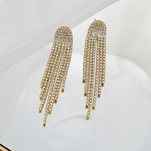 Detailed close-up of golden long tassel earrings with sparkling white rhinestones on silk