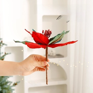 Red velvet poinsettia branch for Christmas tree decoration being held by a hand