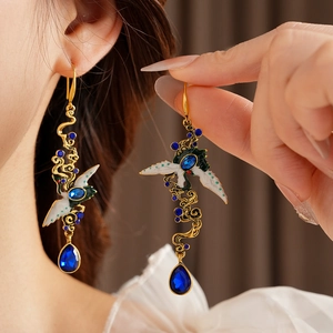 Detail of vintage gold crane earrings with blue teardrop gemstone on a model