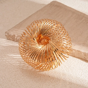 Minimalist geometric hollow spring bangle in polished gold metal on a textured background