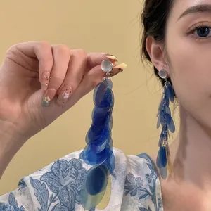 Detail showing long blue sequin tassel earrings with round grey stone studs worn by model