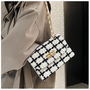 Close-up of a black and white plaid tweed crossbody bag with golden chain on a model