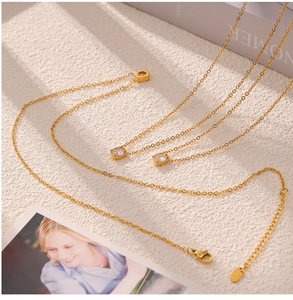 Detailed macro view of gold chain necklaces featuring square zircon pendants on white background