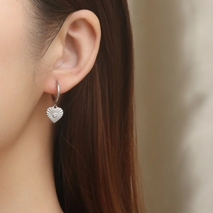 Close-up of silver heart-shaped woven earring with central zircon on model ear