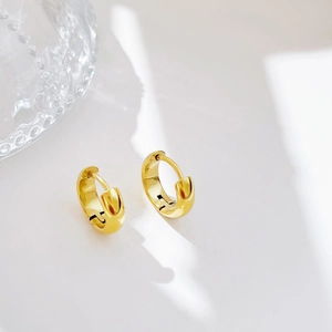 Polished gold huggie hoop earrings with high mirror finish on minimalist cream background