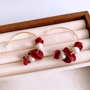 Elegant gold wire earrings with red resin flower petals and white pearls in a jewelry box
