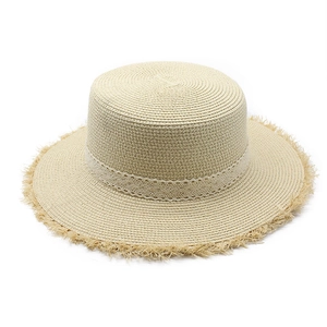 Close-up of beige straw flat top hat featuring white lace ribbon and frayed fringe edges