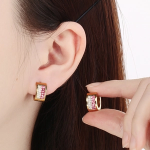 Detail of pink and white rhinestones on a wide gold stainless steel hoop earring
