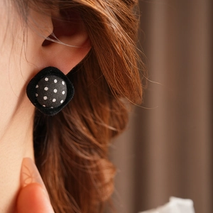 Detail of a vintage-style black fabric earring with white polka dots on model ear