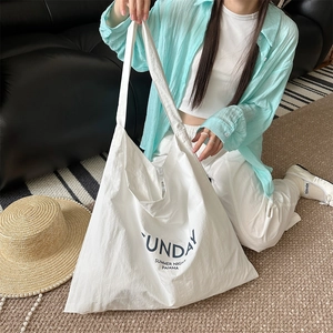 Close-up of white canvas tote bag with blue Sunday Summer Night text on a sofa