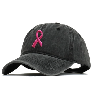 Close-up of pink ribbon embroidery on washed black cotton baseball cap with vintage texture