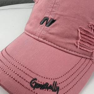 Detail of embroidered N logo and vintage distressed fabric on pink baseball cap
