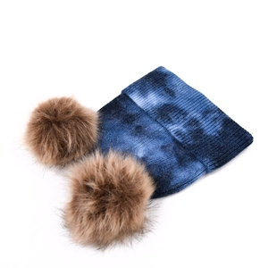 Détails du tricot d'un bonnet tie-dye bleu avec deux pompons en fausse fourrure
