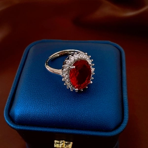 Macro view of oval red zircon ring with white crystal halo in silver-toned setting