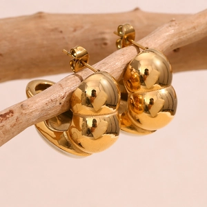 Détail de boucles d'oreilles gouttes dorées 18 carats suspendues à une branche bois