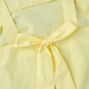 Detail of light yellow summer dress showing the bow tie and wide shoulder strap texture