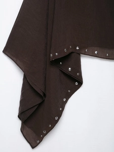 Detail of dark brown fabric showing round silver metal studs on asymmetrical hem edges