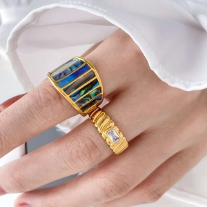 Detailansicht goldener Ringe mit Abalone-Inlay und rechteckigem Zirkon am Finger getragen