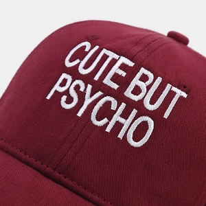 Detail of burgundy baseball cap featuring white CUTE BUT PSYCHO letter embroidery