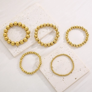 Five-piece set of golden beaded elastic bracelets with various bead sizes on white stone