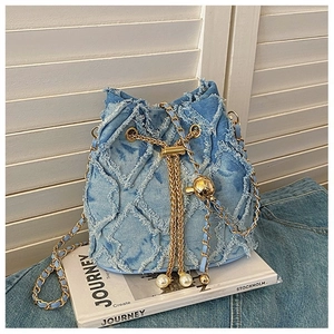 Detail of blue denim bucket bag with gold chain and pearl drawstring on a book