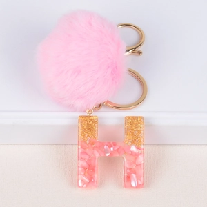 Close-up of pink pompom and resin letter H keychain with gold foil and shell flakes
