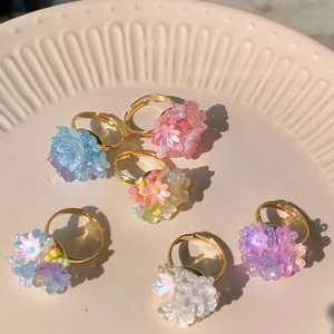 Detail of six colorful floral beaded rings with gold adjustable open bands on a ceramic tray