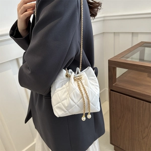 White quilted bucket bag with gold chain strap and pearl accents shown on shoulder