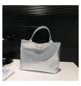 Close-up of the metallic silver woven texture and cylindrical handles on a tote bag