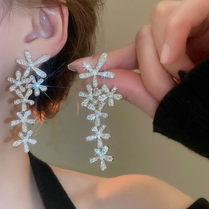 Macro shot of silver tassel earrings with flower designs and sparkling crystals on model