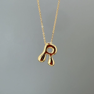 Close-up of golden letter R pendant with molten texture on a minimalist O-chain necklace