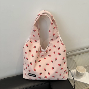 Pink corduroy tote bag with strawberry print and black fashion label on black sofa
