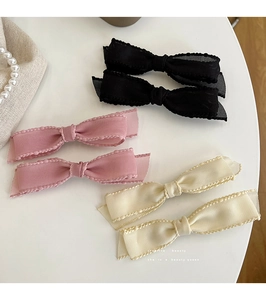 Detail of layered ribbon bow hair clips in black, pink, and beige with wavy edges