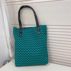 Detail of geometric pattern tote bag with green jacquard fabric and black leather handles