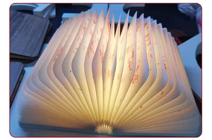 Detailed view of the illuminated wooden book lamp showing warm light and paper pages