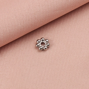 Detailaufnahme einer silbernen Schneeflocken-Abstandsperle für DIY-Schmuck auf Stoff