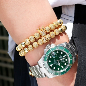 Macro shot of gold beaded bracelets with a crown charm paired with a luxury green watch