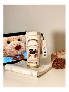 Close-up of cream coffee tumbler with cute black cat illustration and fabric carry strap