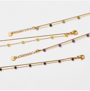 Detail of four stainless steel layered anklets featuring green, yellow, and purple beads