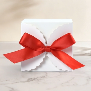Detail view of a white square gift box with scalloped edges and a vibrant red ribbon bow