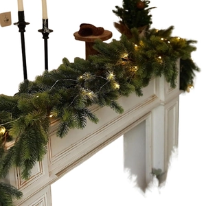 Lush PE artificial pine needle garland with warm LED lights on a classic fireplace