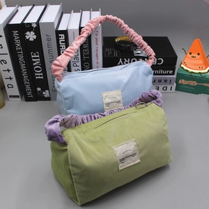 Detail of corduroy handbags in blue and green with ruffled handles and zipper closure