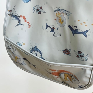 Detail of waterproof baby bib featuring ocean prints and a large crumb catcher pocket