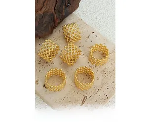 Close-up of six gold rings with hollow mesh weave and crystals on textured stone