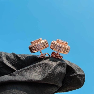 Detail of rose gold hip hop stud earring with zircons held against a blue sky
