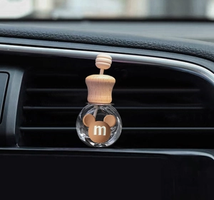 Close-up of a round glass car perfume bottle with wooden cap and brown mouse head detail
