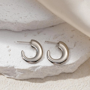 Detailed view of silver C-shaped chunky hoop earrings on a textured stone and silk background