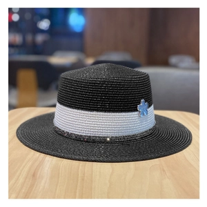 Dettaglio di un cappello di paglia nero con nastro bianco e fiore blu su legno