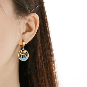 Close-up of model wearing gold enamel earrings with palm tree and dolphin ocean motif