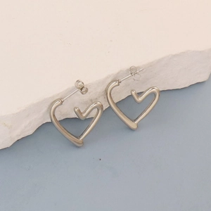Detail of silver heart-shaped earring with organic curves on a textured stone surface